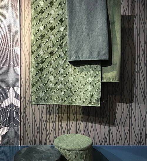 Muted blue and green textiles hanging in front of a grey geometric wallpaper. Carnegie