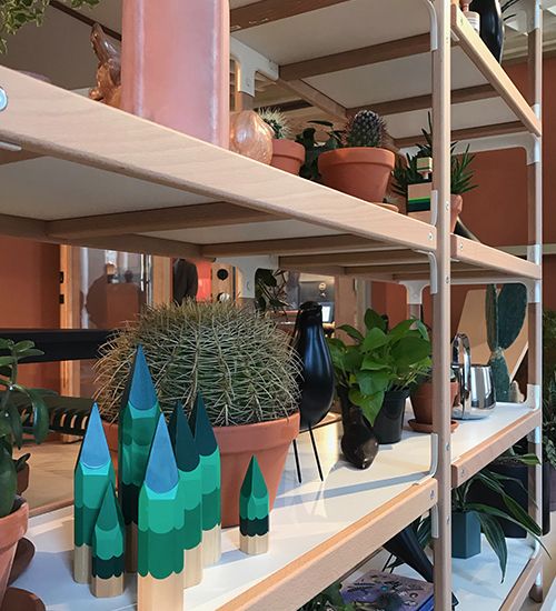 Potted cacti littered among pale pink and blue-green odds and ends on a shelf. Herman Miller