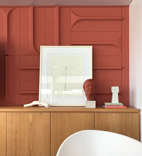 Framed art print and bust in front of a terra cotta-colored sculptural wall. Interface