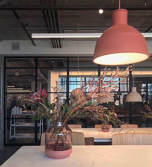 Flower arrangement on a table under a pinky-orange pendant light. Muuto