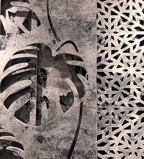 Two fabric panels with concrete texture. The front panel has a bold monstera leaf pattern, while the back panel has a snowflake-like geometric cut-out pattern. Buzzispace