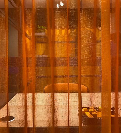 Orange translucent curtain obscuring a workspace with desk and chair. Buzzispace