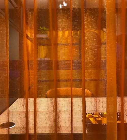 Orange translucent curtain obscuring a workspace with desk and chair. Buzzispace