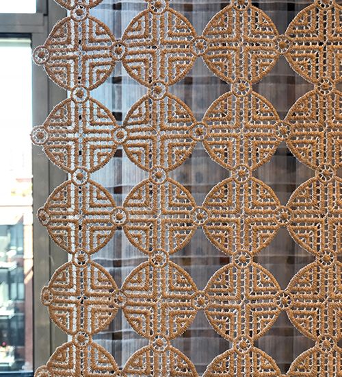 Embroidered textile in a Greek key-like pattern in front of a window.