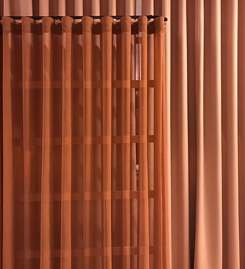 Terra cotta fabric curtain in panes against a solid curtain in the same color. Haworth.
