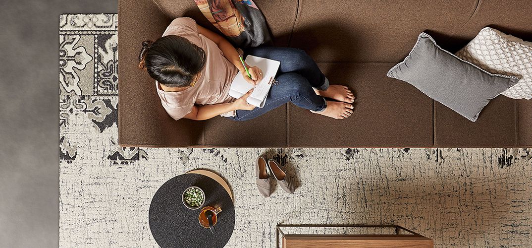 Overhead perspective of a woman on a couch. She's taken off her shoes and her bare feet, coffee cup, and seated position indicate her comfort in this workspace.