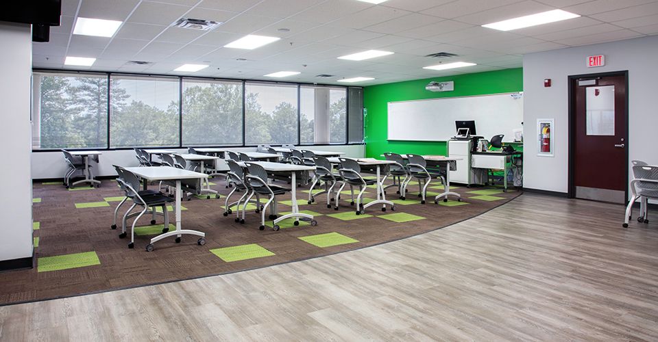 Open classroom space with movable desks, green walls, and brown and green carpet tiles on the floor..