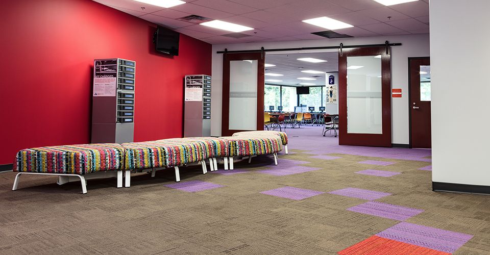In-between space that has graphic upholstered benches and purple carpet tile that provides wayfinding into a classroom space.