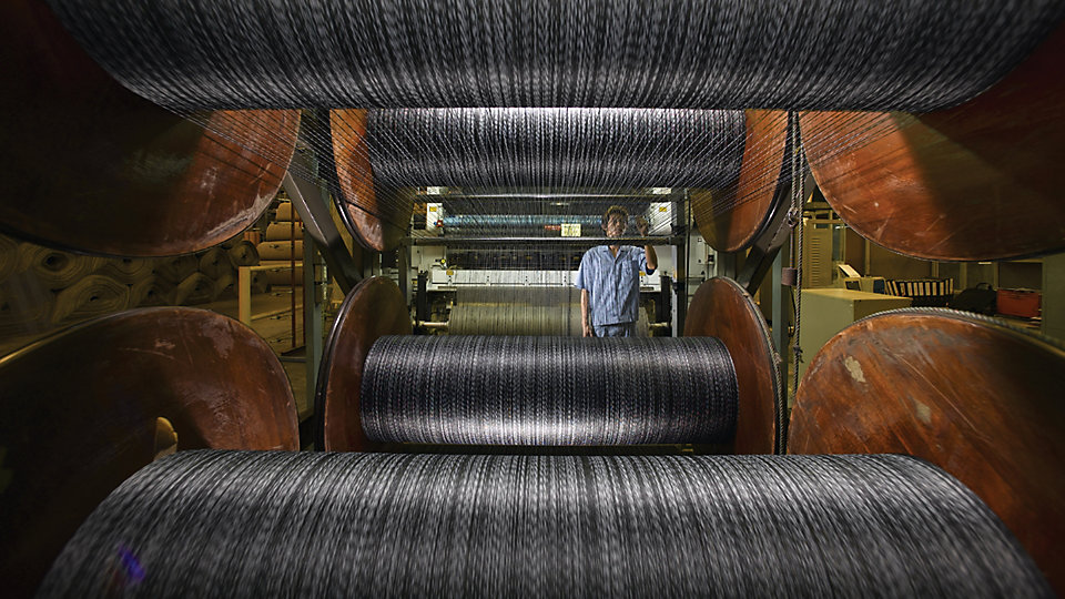 A tufting machine operator watches for irregularities as yarn is pulled from spools.